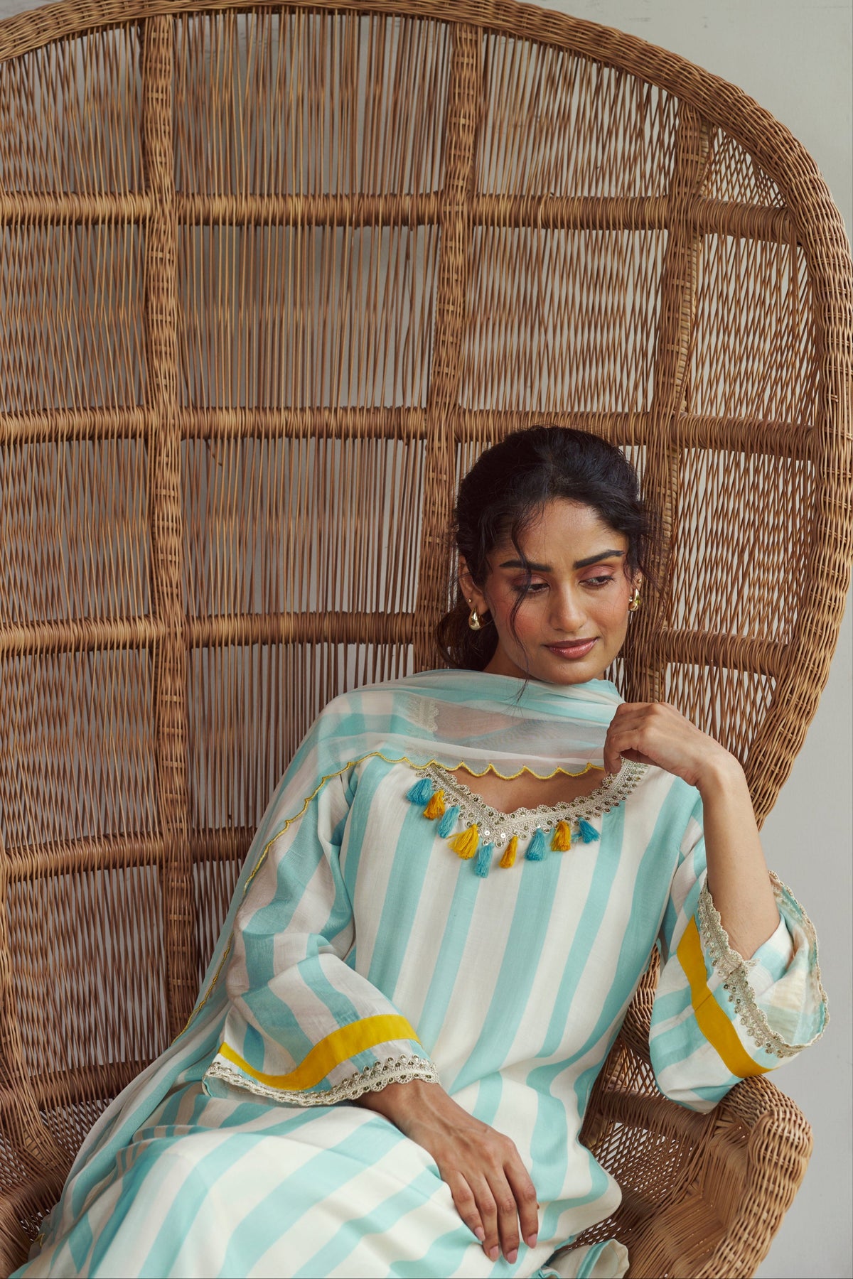 Woman in a striped dress sitting on a wicker chair against a plain background