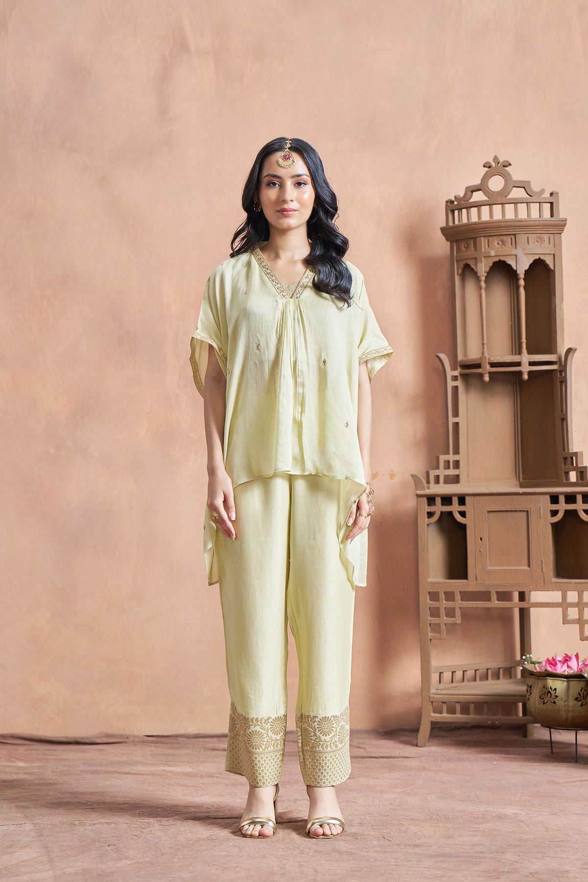 A woman wearing a lime green tussar silk co-ords set with zari work, including a V-neck top with embroidered lace and a brocade silk inner, along with matching pants. 