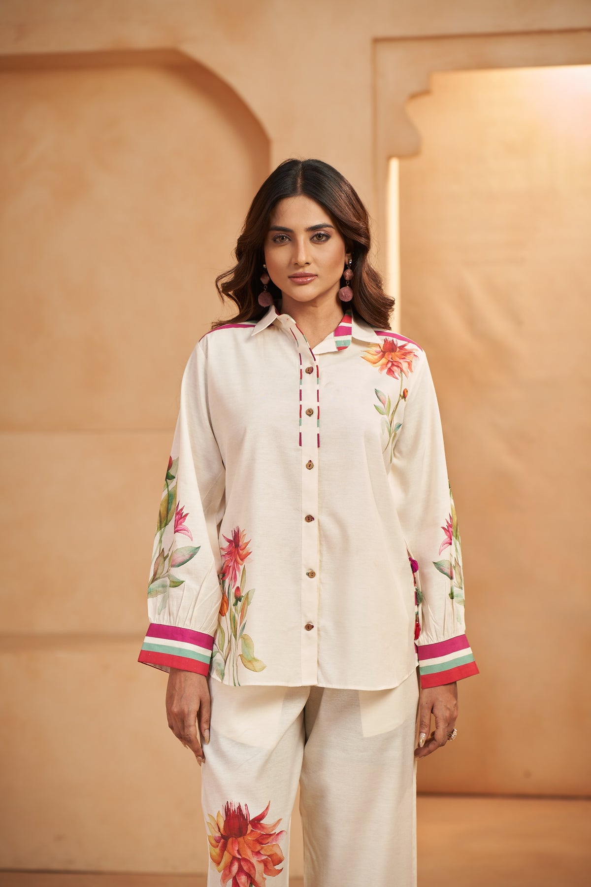 Woman wearing a cream-colored outfit with floral patterns against a beige wall.