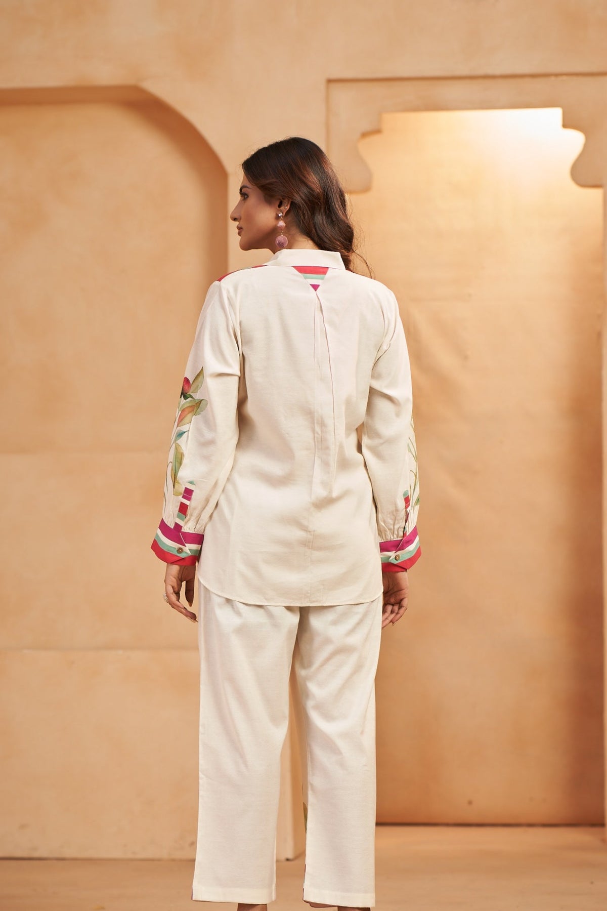 Woman in a white outfit standing in a room with beige walls and a light fixture.