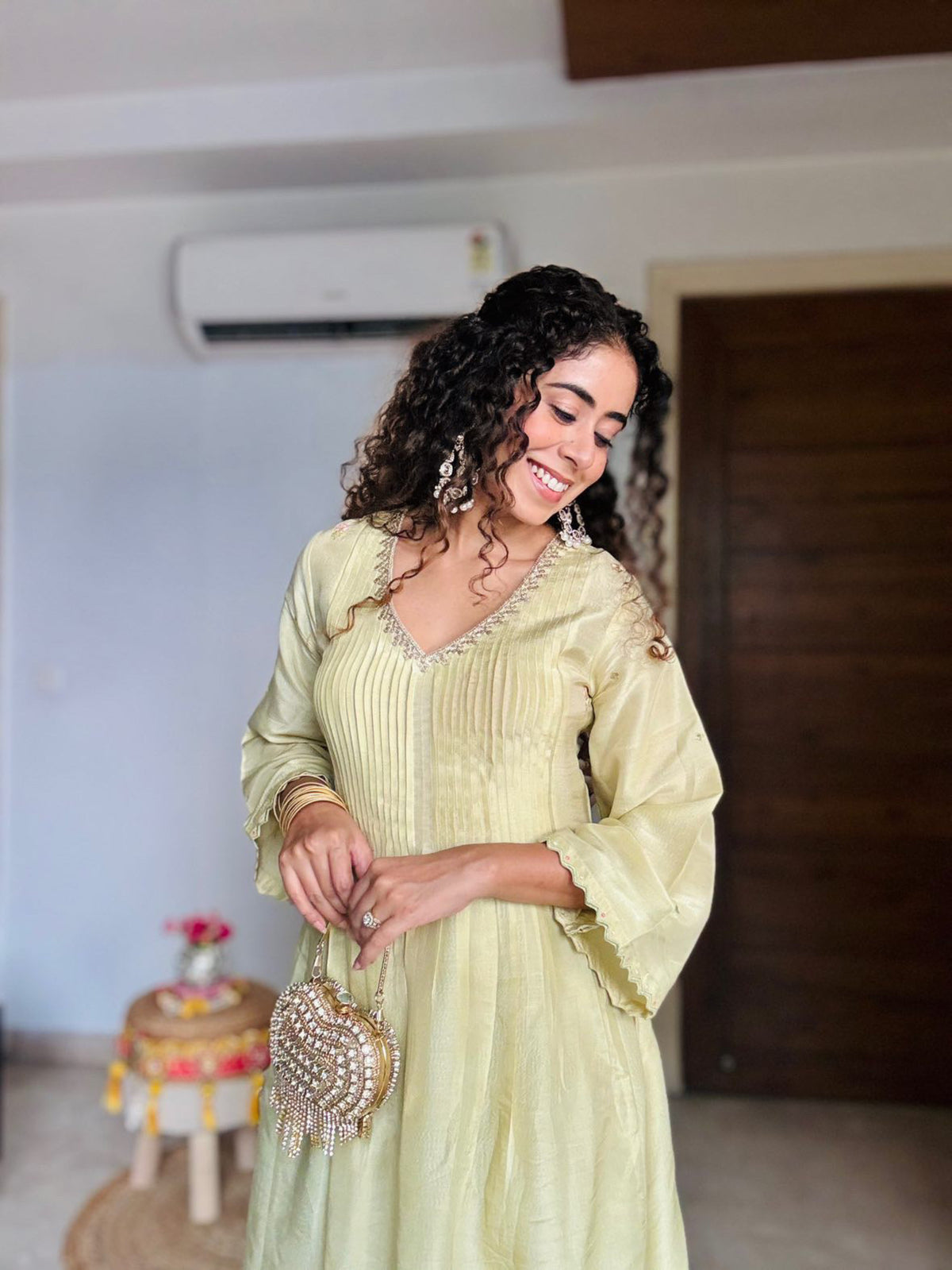 A woman wearing a pista green pleated kurta set with embroidered lace and scalap sleeves, paired with palazzo pants, standing indoors.
