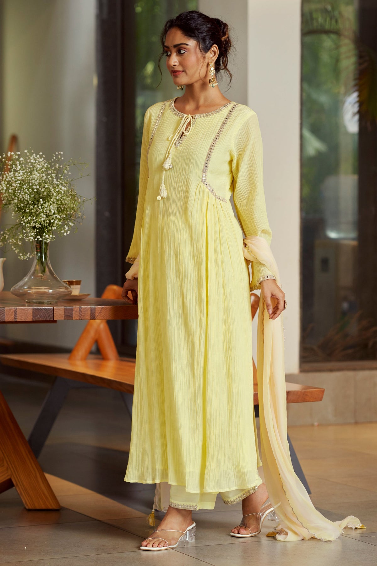 Woman in a light yellow kurta with a white dupatta standing indoors.