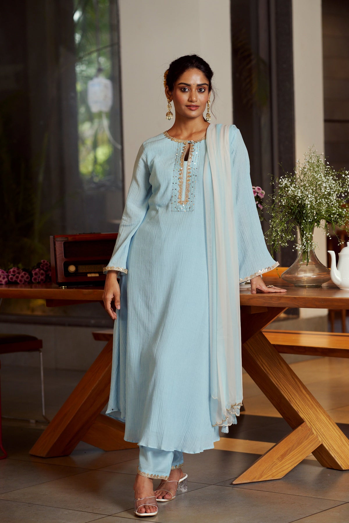 Woman in a light blue traditional outfit standing in a modern interior setting.