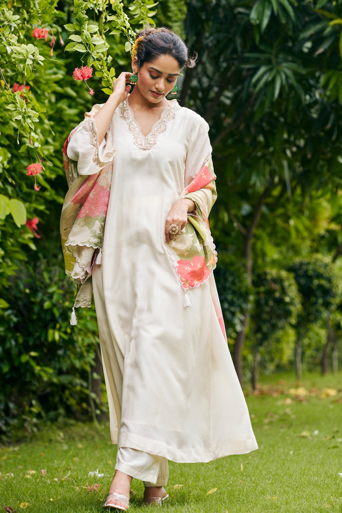 Woman in a white traditional outfit standing in a lush green garden.
