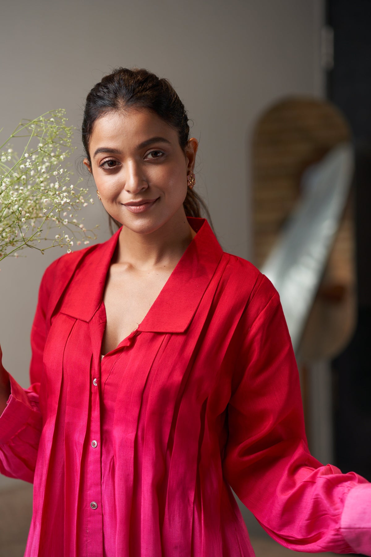 Woman wearing a bright pink shirt holding a plant indoors